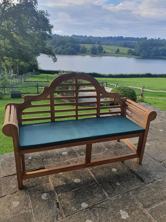 Lutyens teak bench with green bench cushion beside a lake