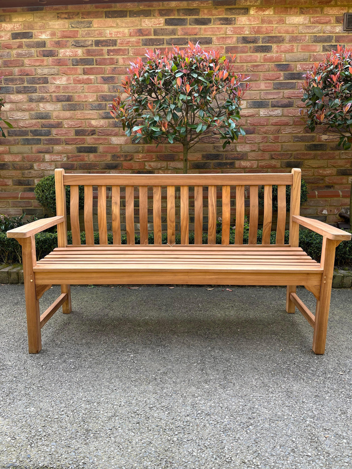 Solid teak wave back bench, front view against a brick wall