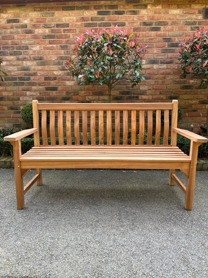 Solid teak wave back bench, front view against a brick wall