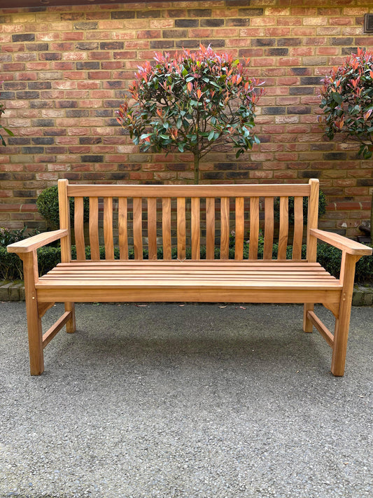 Solid teak wave back bench, front view against a brick wall