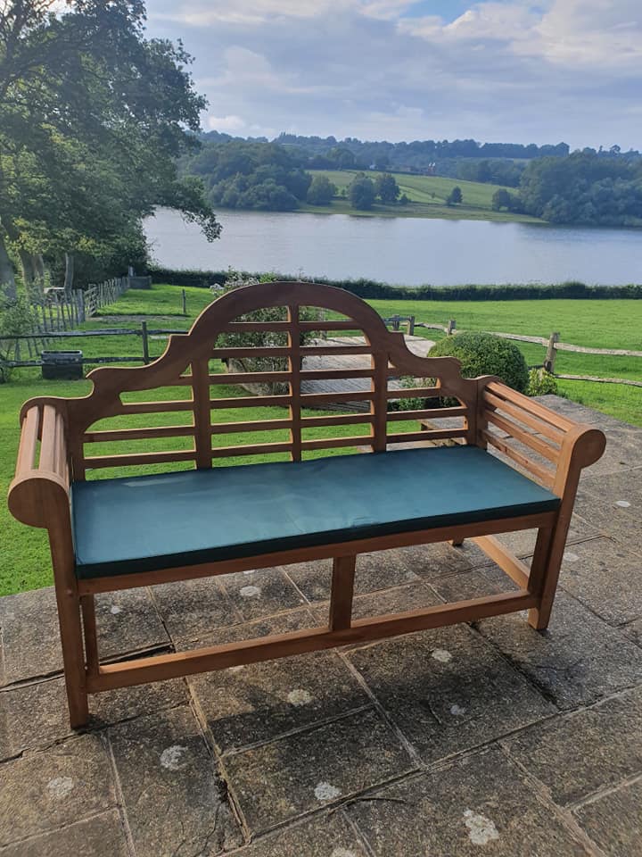 Lutyens teak bench with green bench cushion beside a lake