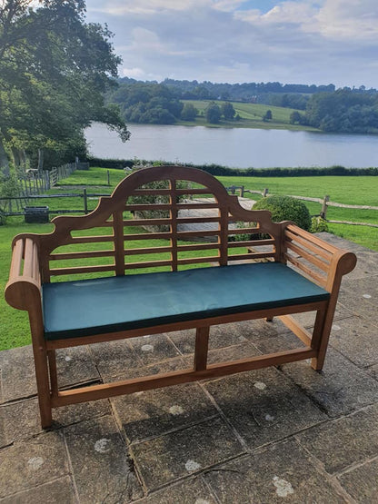 Lutyens teak bench with green bench cushion beside a lake